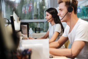 Side View Of Coworkers Sit By The Table In Headphones