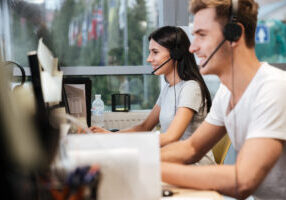 Side View Of Coworkers Sit By The Table In Headphones