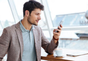 Man In Jacket Texting Message On Smartphone While Sitting Indoors